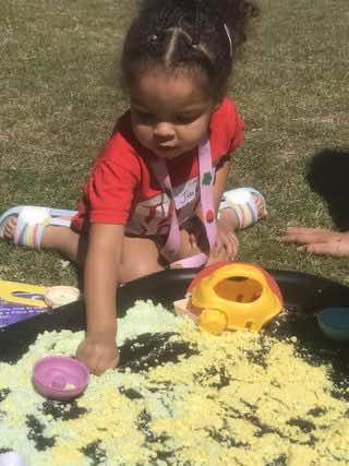 A small child uses a Tuff Tray to explore writing skills during an outdoors play activity.