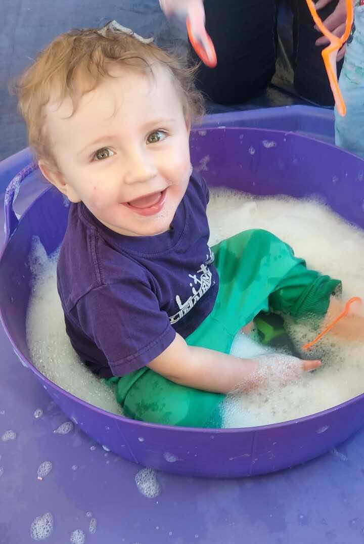 A child plays in a bucket of water with bubbles