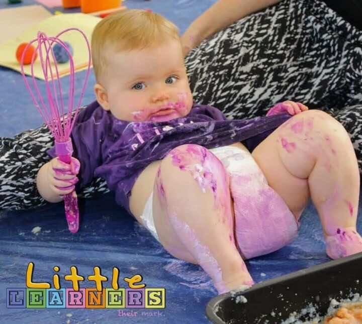 A baby covered in pink icing plays at a messy play session run by a Little Learners franchisee