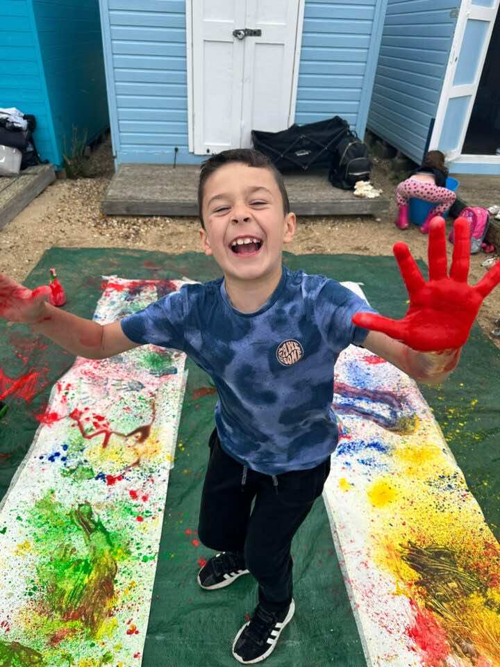 A child laughs and holds his paint stained hands upto the camera