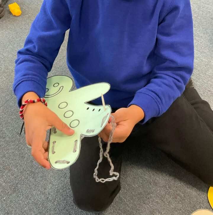 Child threading wool around the edge of a gingerbread man outline 