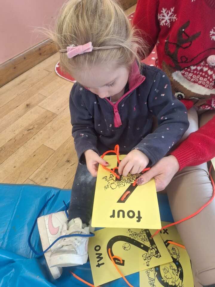 Little girl threads a shoelace through a plastic number