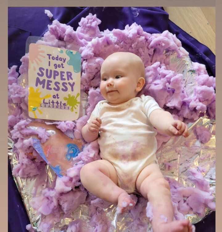 A baby plays in a sensory tray of foam at a Little Learners class