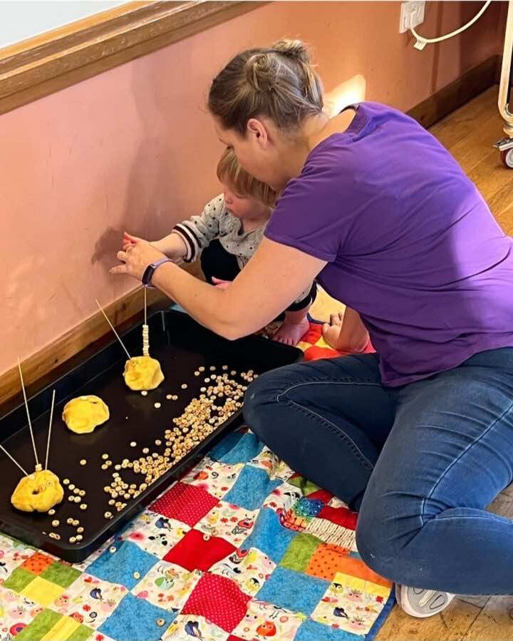 Adult helps child thread cereal onto spaghetti