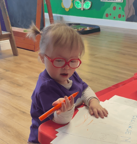 A girl with down syndrome practices mark making with an orange pen at Little Learners UK 