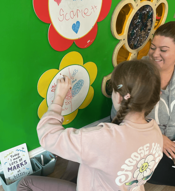 A child attends a SEND session at Little Learners Playspace Ashington. A young girl draws on a flower shaped wipe board. 