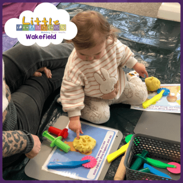 A child kneels on the floor with her finger poking some yellow play dough during a Little Learners Wakefield messy play class.