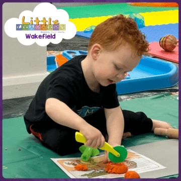 A child sits on the floor playing with orange play dough using a cutting wheel during a Little Learners Wakefield messy play class.