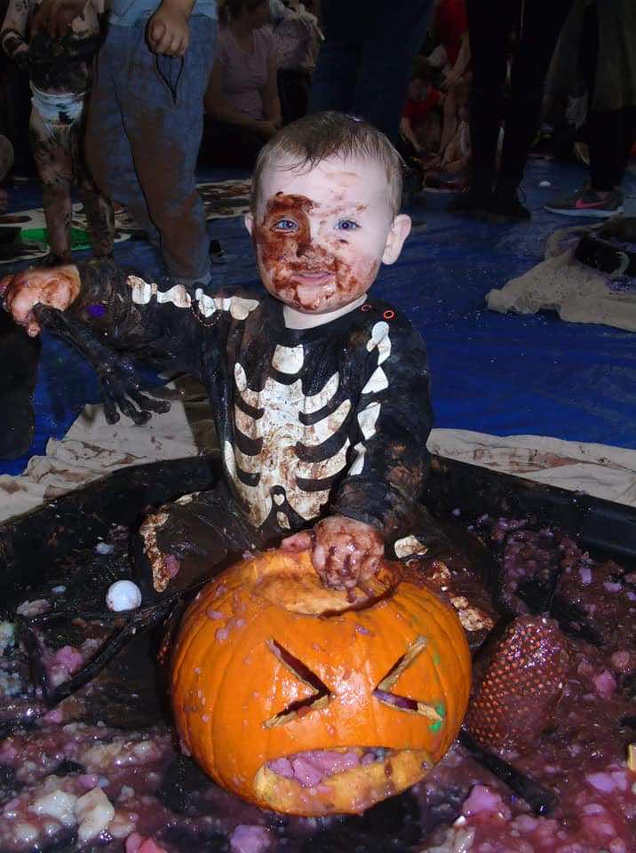 Little Learners Halloween Messy Play Events 2024 - a child dressed as a skeleton plays with a pumpkin